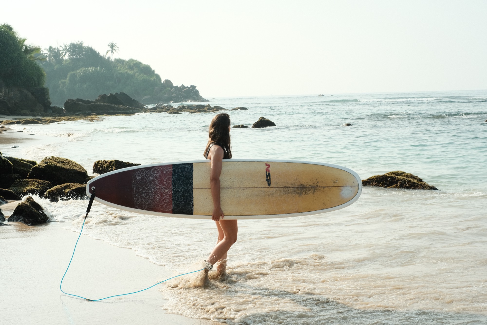 Alexandra walking into the sea with a longboard on Sri Lanka's south coast
