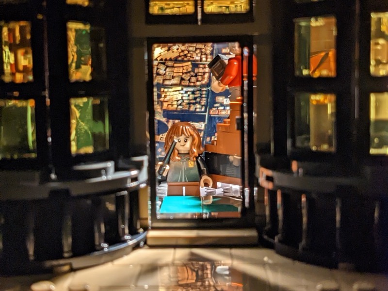 A Lego minifigure framed in a warmly lit doorway between dark shelves